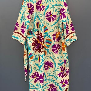 May include: A cream-colored robe with a floral pattern in shades of purple, teal, orange, and yellow. The robe has a tie belt and long sleeves.