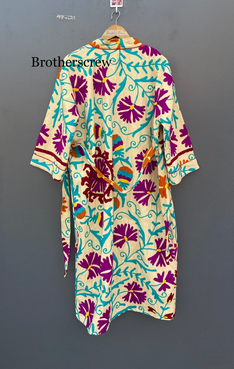 May include: A cream-colored robe with a floral pattern in shades of purple, teal, orange, and yellow. The robe has a tie belt and long sleeves.