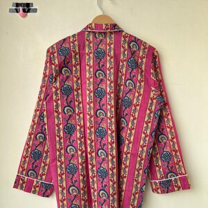 May include: A pink pajama top with vertical stripes and floral patterns in blue and beige. The long-sleeved top has white trim along the collar and cuffs, hanging on a wooden hanger.