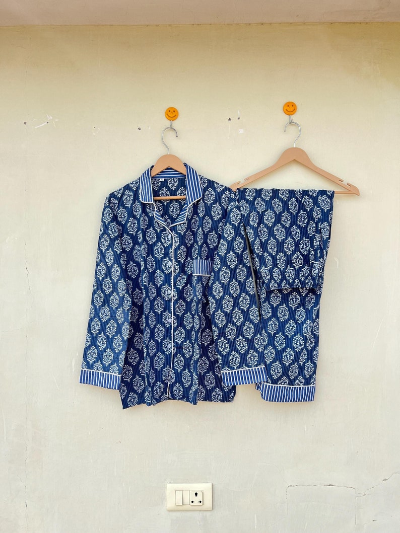 K&ouml;nnte beinhalten: Ein blaues und wei&szlig; gemustertes Pyjama-Set mit einem lang&auml;rmeligen Oberteil und einer Hose. Das Set h&auml;ngt an zwei Holzb&uuml;geln.