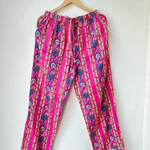 May include: Pink pajama pants with vertical stripes and floral patterns in blue, beige, and red. The pants have a drawstring waist and white trim along the cuffs. The fabric appears to be lightweight.
