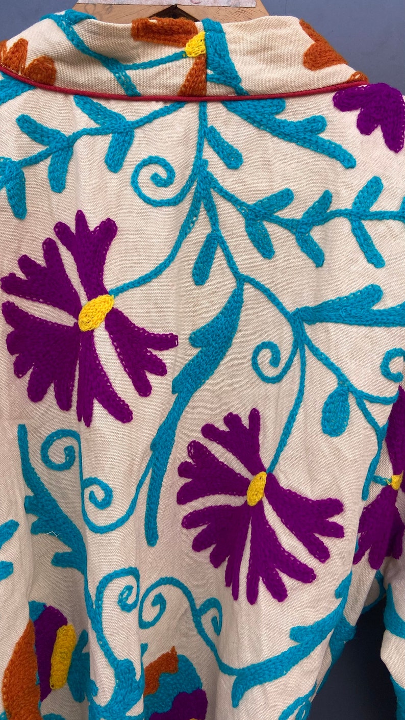May include: White cotton fabric with colorful embroidery. The embroidery features a floral pattern with purple, blue, yellow, and orange thread.