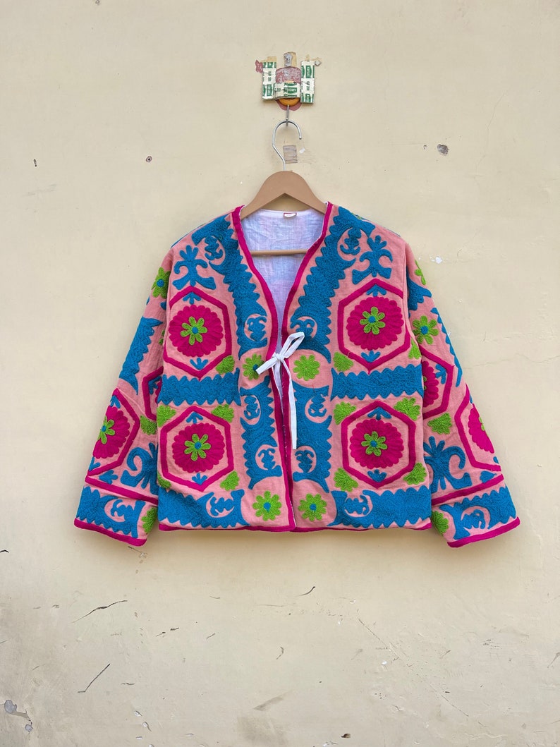 Puede incluir: Una chaqueta bordada de color rosa y azul con un patr&oacute;n geom&eacute;trico. La chaqueta tiene un cierre de corbata en el cuello.