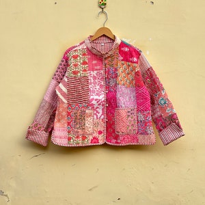May include: A pink quilted jacket with a patchwork design. The jacket has a button closure and long sleeves.