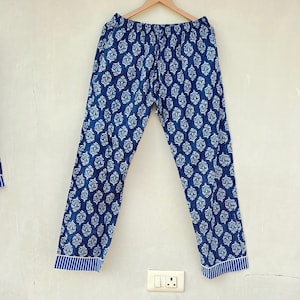 K&ouml;nnte beinhalten: Blaue Baumwollhose mit wei&szlig;em Blumenmuster. Die Hose hat einen Kordelzugbund und einen gestreiften Saum am unteren Ende.