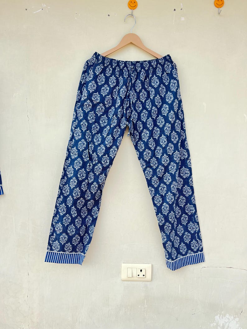 K&ouml;nnte beinhalten: Blaue Baumwollhose mit wei&szlig;em Blumenmuster. Die Hose hat einen Kordelzugbund und einen gestreiften Saum am unteren Ende.
