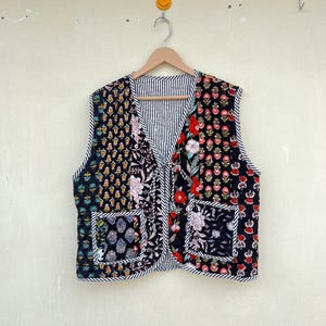 May include: A black quilted vest with a floral print and a striped lining. The vest has two pockets on the front and a V-neck.