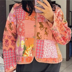 May include: A pink and orange patchwork quilted jacket with a floral and tiger print. The jacket has a button closure and a mandarin collar.