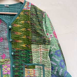 Puede incluir: Una chaqueta acolchada verde con un dise&ntilde;o de patchwork. La chaqueta tiene un cierre de bot&oacute;n y dos bolsillos. La tela es una mezcla de diferentes patrones y colores, incluyendo verde, azul, rosa y amarillo.