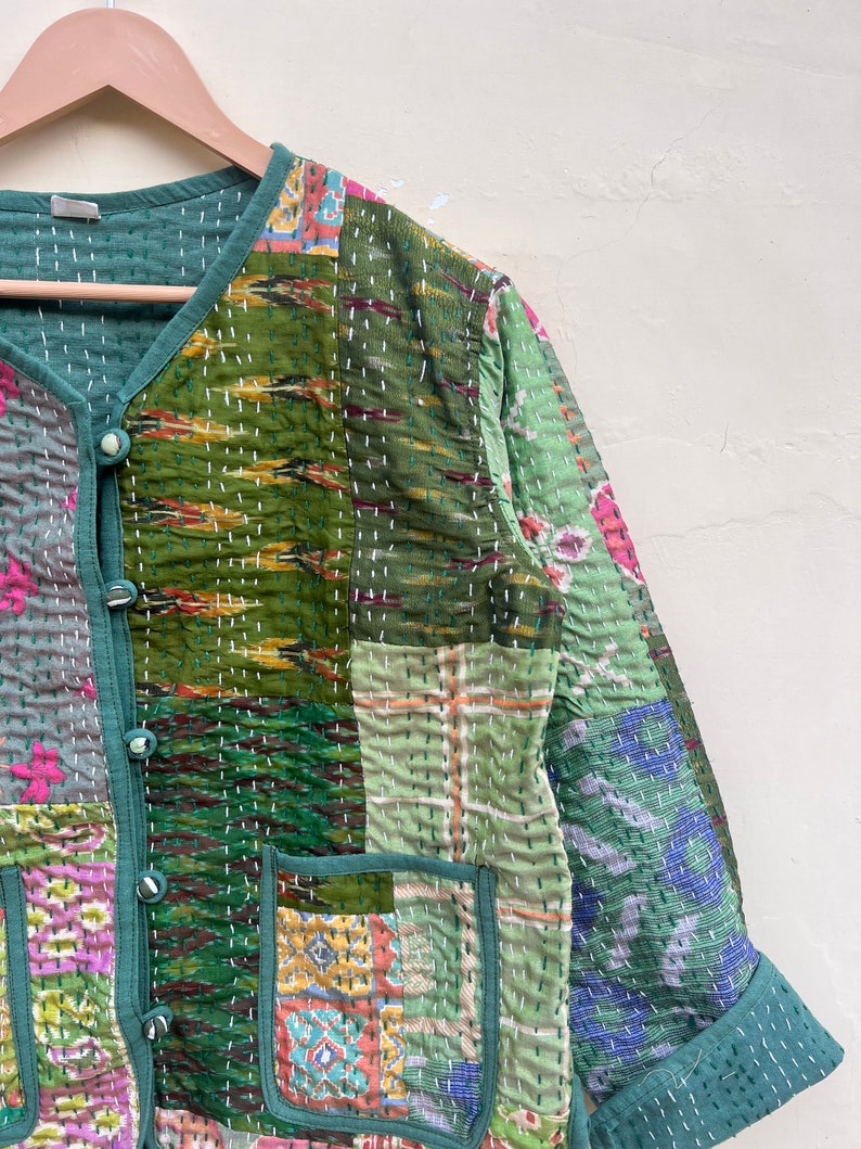 Puede incluir: Una chaqueta acolchada verde con un dise&ntilde;o de patchwork. La chaqueta tiene un cierre de bot&oacute;n y dos bolsillos. La tela es una mezcla de diferentes patrones y colores, incluyendo verde, azul, rosa y amarillo.