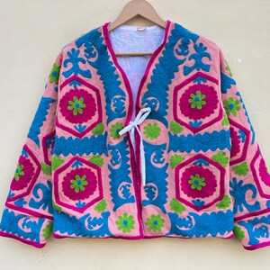 Puede incluir: Una chaqueta rosa bordada con cierre de lazo. El bordado presenta un patr&oacute;n geom&eacute;trico en tonos de rosa, azul y verde.