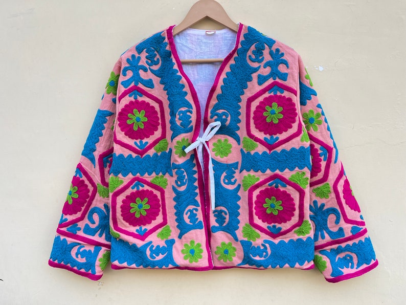 Puede incluir: Una chaqueta rosa bordada con cierre de lazo. El bordado presenta un patr&oacute;n geom&eacute;trico en tonos de rosa, azul y verde.