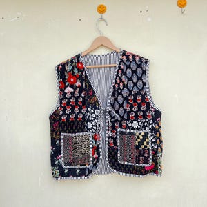 May include: A black quilted vest with a floral print and a tie closure. The vest has two pockets and a striped lining.