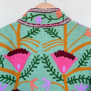 May include: A mint green jacket with embroidered flowers in shades of pink, orange, purple, and green.