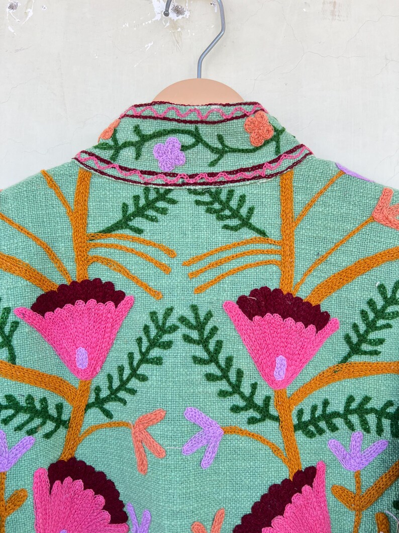 May include: A mint green jacket with embroidered flowers in shades of pink, orange, purple, and green.