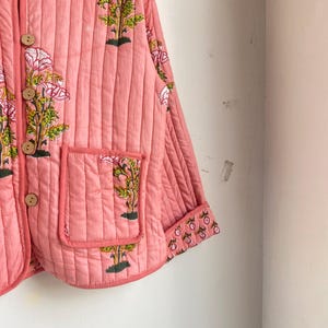 Pu&ograve; includere: Giacca trapuntata rosa chiaro con stampa floreale. La giacca presenta una chiusura con bottoni, due tasche e un motivo floreale sui polsini. Il design floreale comprende fiori rosa e foglie verdi. La giacca &egrave; realizzata in un tessuto trapuntato morbido.