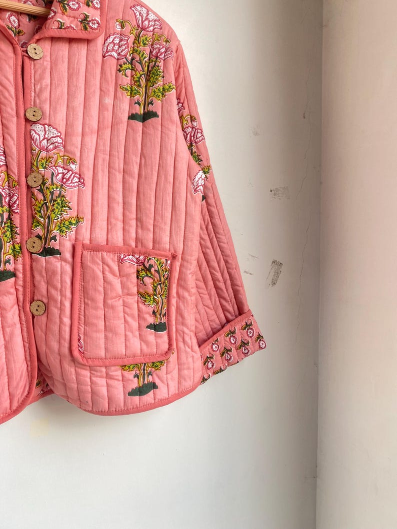 Pu&ograve; includere: Giacca trapuntata rosa chiaro con stampa floreale. La giacca presenta una chiusura con bottoni, due tasche e un motivo floreale sui polsini. Il design floreale comprende fiori rosa e foglie verdi. La giacca &egrave; realizzata in un tessuto trapuntato morbido.