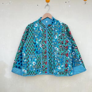 Può includere: Una giacca trapuntata con motivo verde e blu, colletto alla coreana e maniche lunghe. La giacca ha una chiusura con bottoni e una fodera a righe.