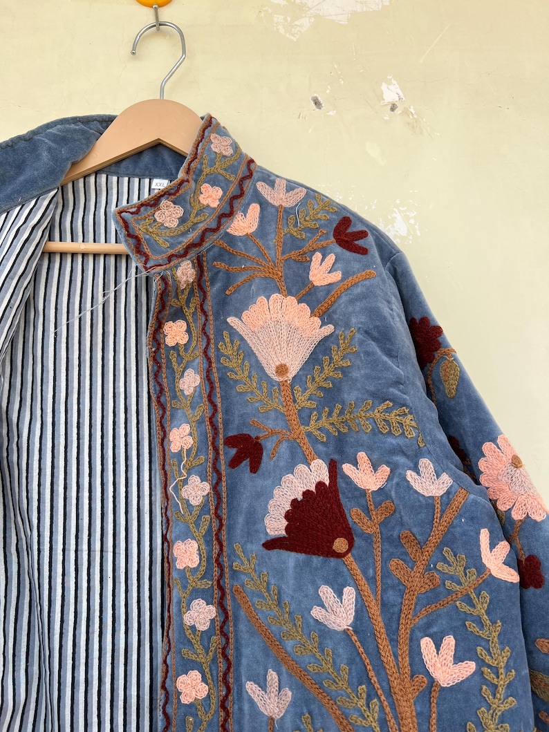 May include: A blue velvet jacket with intricate floral embroidery in shades of pink, brown, and red. The jacket has a striped lining and a mandarin collar.
