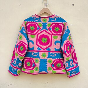 Puede incluir: Una chaqueta rosa de manga larga con un patr&oacute;n geom&eacute;trico bordado en rosa, verde y azul.