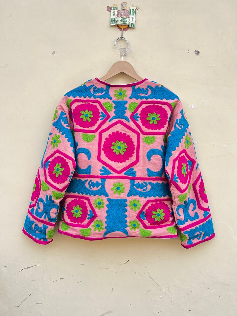 Puede incluir: Una chaqueta rosa de manga larga con un patr&oacute;n geom&eacute;trico bordado en rosa, verde y azul.