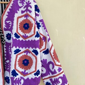 May include: A white jacket with purple and blue embroidery. The embroidery features geometric patterns and floral designs.