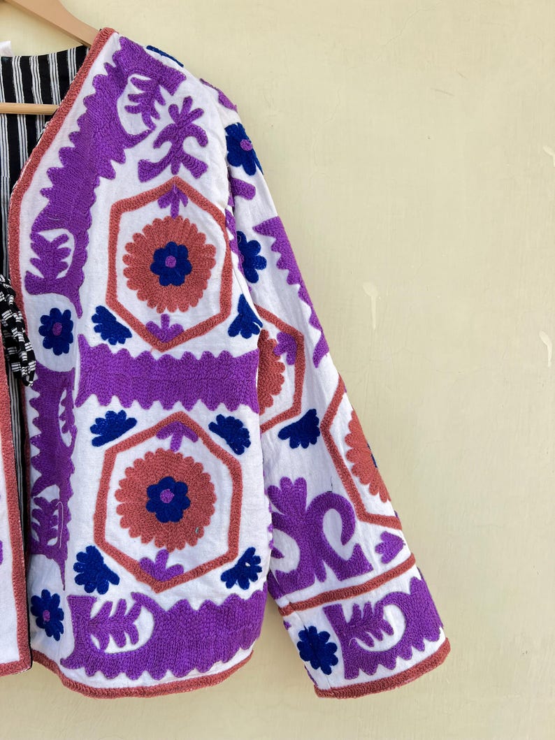 May include: A white jacket with purple and blue embroidery. The embroidery features geometric patterns and floral designs.