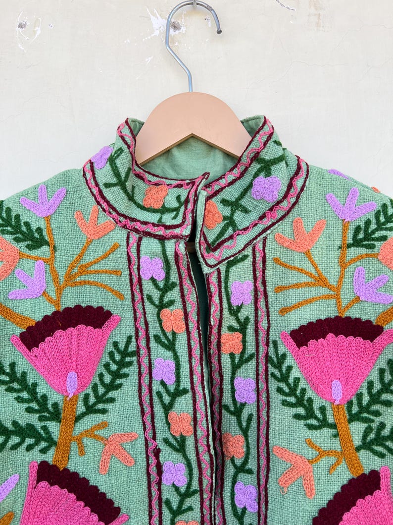 May include: A green embroidered jacket with pink, orange, and purple floral designs. The jacket has a high collar and a button closure.