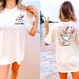 May include: An off-white short-sleeve t-shirt featuring a small graphic of a pig and a rooster on the left chest with the text Custom Name below it, and a large, colorful floral graphic with the same pig and rooster on the back.