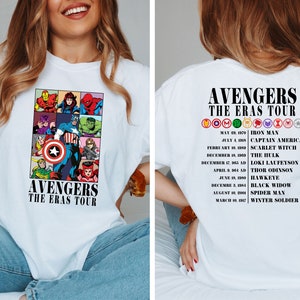 May include: White t-shirt with a graphic of the Avengers characters and the text "Avengers The Eras Tour". The back of the shirt has a list of the Avengers characters and their first appearances.