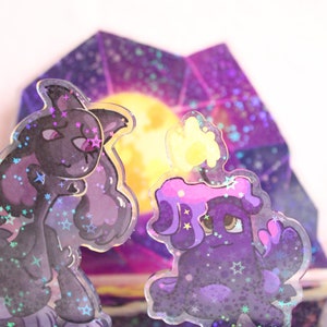 May include: Two holographic character stickers with a purple and black colour scheme. The characters are set against a background of a holographic purple and blue gem with a yellow moon.