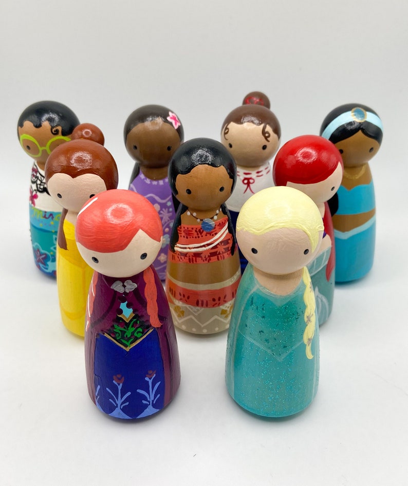 Puede incluir: Una colecci&oacute;n de mu&ntilde;ecas de madera pintadas a mano, cada una representando un personaje diferente con rasgos faciales, peinados y atuendos coloridos &uacute;nicos. Las mu&ntilde;ecas est&aacute;n dispuestas en grupo, mostrando una variedad de dise&ntilde;os y temas.