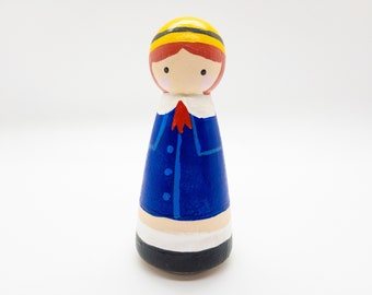 May include: A hand-painted wooden peg doll with red hair, a yellow hat, a blue coat, and white collar. The doll is wearing a red bow tie.