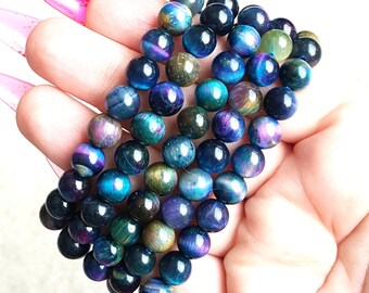 Puede incluir: Una hebra de cuentas de ojo de tigre iridiscente azul, verde y morado. Las cuentas son redondas y tienen un acabado liso y pulido.