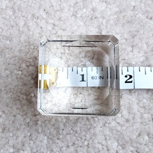Puede incluir: Un cuadrado de vidrio transparente con una cinta m&eacute;trica que muestra 1 pulgada. La cinta es parcialmente visible en el vidrio.
