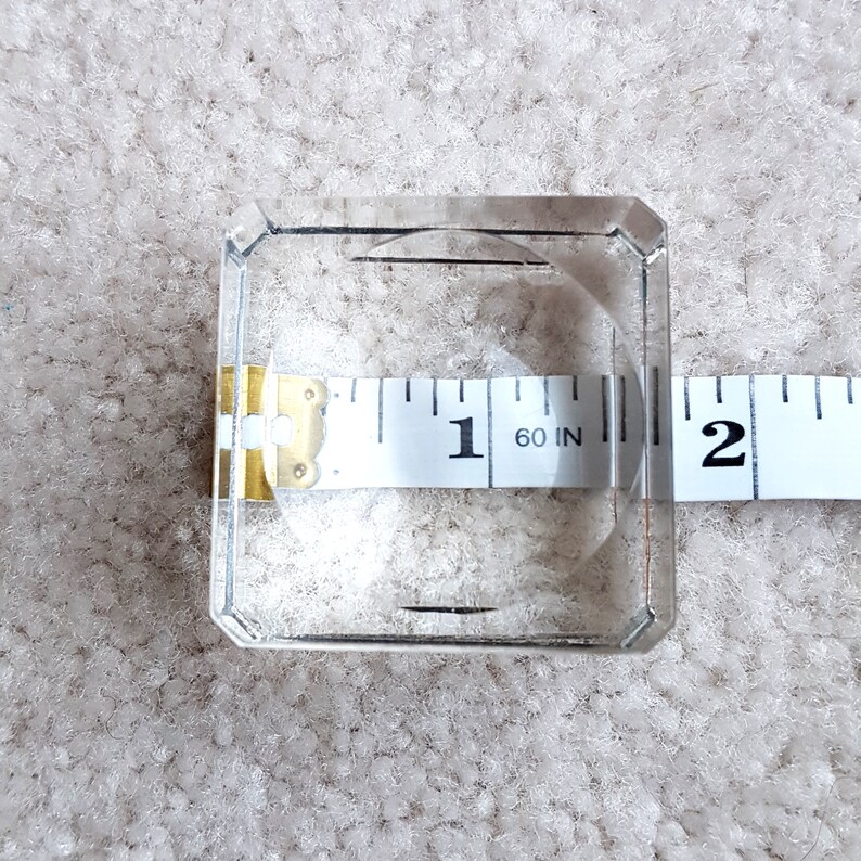 Puede incluir: Un cuadrado de vidrio transparente con una cinta m&eacute;trica que muestra 1 pulgada. La cinta es parcialmente visible en el vidrio.