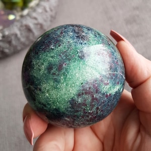 May include: A green and purple sphere with a sparkly finish. The sphere is made of natural stone and has a unique, marbled pattern.