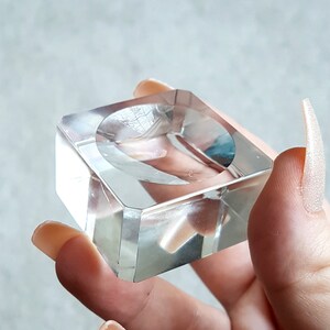 Puede incluir: Un expositor de cristal transparente con una base cuadrada y una hendidura circular en la parte superior. El expositor est&aacute; hecho de cristal transparente y tiene un acabado liso y pulido.