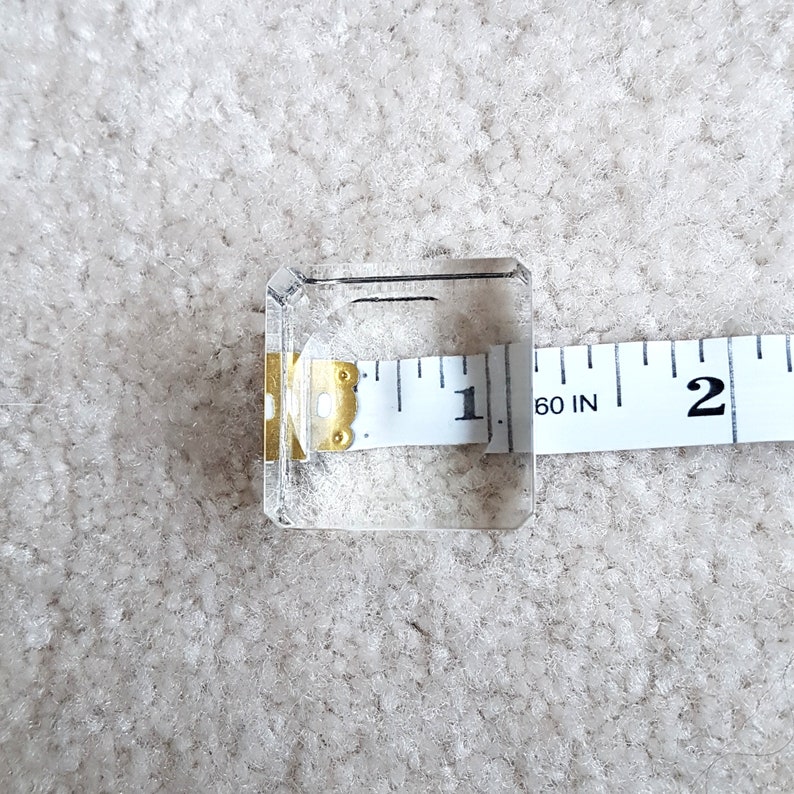 Puede incluir: Un cubo de vidrio transparente con una cinta m&eacute;trica encima. La cinta m&eacute;trica indica "60 IN" y tiene marcas para pulgadas.