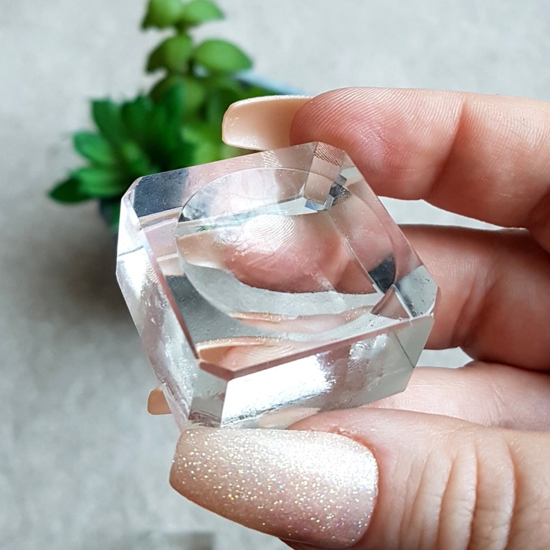 Puede incluir: Un porta anillos de cristal transparente con una base cuadrada y una abertura redonda en el centro. El porta anillos est&aacute; hecho de vidrio transparente y tiene un acabado liso y pulido.