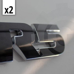 May include: Two silver-colored metal car emblems that say "RS" in a bold, three-dimensional font.
