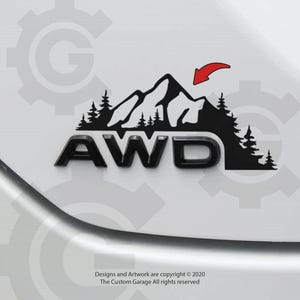 May include: Black and white decal of a mountain range with trees and the word "AWD" in black letters. The decal is on a white surface.