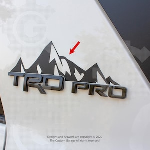 Peut inclure: Graphique de montagne noir et blanc avec le texte "TRD PRO" en lettres noires. Le graphique est sur une surface blanche.