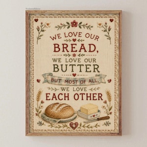 Puede incluir: Una impresión de arte mural enmarcada sobre un fondo de tela texturizada con el texto WE LOVE OUR BREAD, WE LOVE OUR BUTTER BUT MOST OF ALL, WE LOVE EACH OTHER. El diseño incluye ilustraciones de una hogaza de pan, mantequilla y trigo.