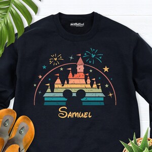 Puede incluir: Sudadera negra con una ilustraci&oacute;n de estilo retro de un castillo con fuegos artificiales y estrellas. El castillo est&aacute; en colores arco&iacute;ris y tiene el nombre "Samuel" impreso debajo.