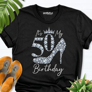 May include: Black t-shirt with the text "It's My 50th Birthday". The number 50 is designed with sparkling gems, and a high heel shoe is also made of gems. A crown is above the number 50.