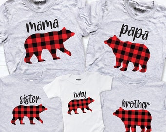 Può includere: Set di cinque magliette grigie con silhouette di orsi a quadri rossi e neri. Le magliette dicono "mamma", "papà", "sorella", "fratello" e "bambino".