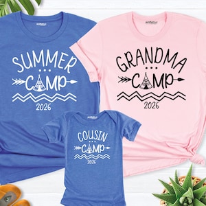 May include: A blue t-shirt with "Summer Camp 2026" text, a pink t-shirt with "Grandma Camp 2026" text, and a blue onesie with "Cousin Camp 2026" text. The text is in white. The shirts and onesie are short-sleeved.