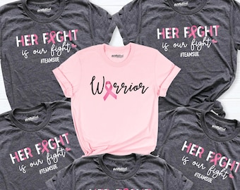 May include: Five t-shirts with pink ribbon designs. Four of the shirts are gray with the text "HER FIGHT is our fight #TEAMSUE". One shirt is pink with the text "Warrior" and a pink ribbon.