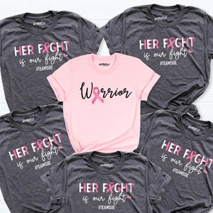 May include: Five t-shirts with pink ribbon designs. Four of the shirts are gray with the text "HER FIGHT is our fight #TEAMSUE". One shirt is pink with the text "Warrior" and a pink ribbon.